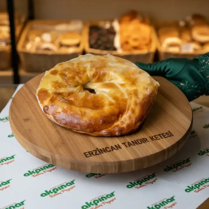 Market tezgâhında yeşil eldivenle tutulan Erzincan tandır ketesi ahşap sunum tahtası üzerinde