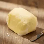 Ahşap masa üzerinde ambalajlı Yayık Kahvaltılık Tereyağı 500 gr, yanında tereyağı bıçağıyla sunulan doğal tereyağı görseli.